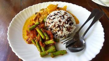 Close up Three color rice with spicy yellow curry with pork and Stir fried pork belly and red curry paste with string bean in white dish on brown wooden background or table with copy space. photo