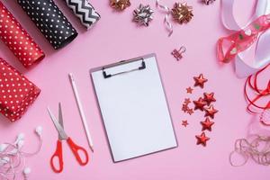 Blank sheet of paper and wrapping materials for christmas presents flat lay on pink background photo