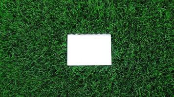 Empty white paper on green grass background. For message flat lay with copy space for text or products presentation. Nature concept, business and lifestyle environment. photo