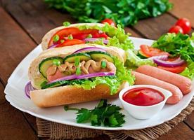 Hot Dog con salsa de tomate, mostaza, lechuga y verduras en la mesa de madera foto