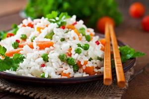 Appetizing healthy rice with vegetables in white plate on a wooden background. photo