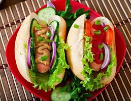 Hot Dog con salsa de tomate, mostaza, lechuga y verduras en la mesa de madera foto