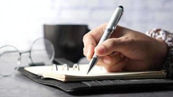 hand- schrijven Aan een planner, een kop van koffie en bril Aan de tafel video