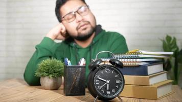 l'homme dort assis à une table avec des livres et une horloge video