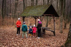 Mother with her kids having rest in autumn forest with roof shelter and picnic table. photo