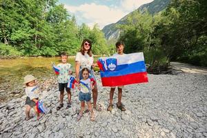 Mother with kids hold slovenian flags in rocky shore of a calm river in Triglav National Park, Slovenia. photo