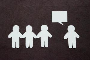 Silhouettes of people cut from white paper on a black background. A group of people stands in front of one person who is speaking speech-bubble. Communication, leadership, teamwork concept photo