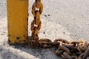 Old rusty yellow chain with large links close-up on a rack on the dock photo