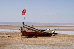 Salt lake in Tunisia Chott el Djerid during a sunny windy day. Largest salt lake in the Sahara Desert. Tourist destination. Travel the world. Boat on the dry lake. Mysterious landscape. photo