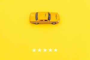 taxi de coche de juguete amarillo y calificación de 5 estrellas aislado sobre fondo amarillo. aplicación de teléfono inteligente del servicio de taxi para buscar en línea llamadas y reservar el concepto de taxi. símbolo de taxi. copie el espacio foto