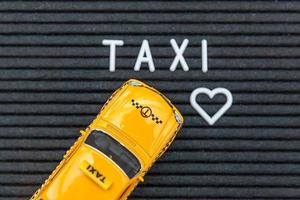 Simply design yellow toy car Taxi Cab model with inscription TAXI letters word on black background. Automobile and transportation symbol. City traffic delivery urban service idea concept. Copy space. photo