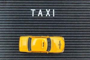 Simply design yellow toy car Taxi Cab model with inscription TAXI letters word on black background. Automobile and transportation symbol. City traffic delivery urban service idea concept. Copy space. photo