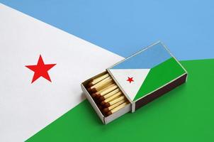 Djibouti flag  is shown in an open matchbox, which is filled with matches and lies on a large flag photo