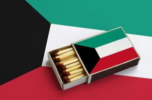 Kuwait flag  is shown in an open matchbox, which is filled with matches and lies on a large flag photo