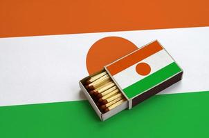 Niger flag  is shown in an open matchbox, which is filled with matches and lies on a large flag photo