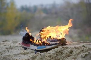 Burning sports sneakers or gym shoes on fire stand on sandy beach coast. Athlete burned out. Physical exertion during training concept photo