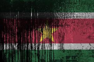 Suriname flag depicted in paint colors on old and dirty oil barrel wall closeup. Textured banner on rough background photo