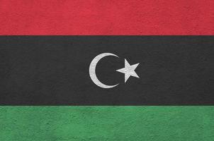 Libya flag depicted in bright paint colors on old relief plastering wall. Textured banner on rough background photo