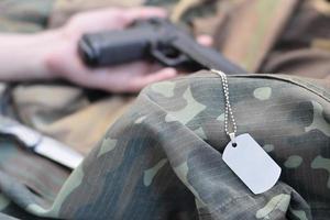 Dog tag with armed hand of dead recruit of Russian army lies on many camouflage clothes photo