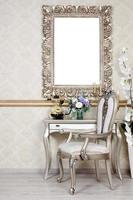 A fragment of a retro interior with a chair and table, on which is a telephone and a vase of flowers. Above the table hangs an empty picture frame for your photo