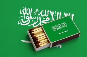 Saudi Arabia flag  is shown in an open matchbox, which is filled with matches and lies on a large flag photo