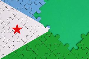 Djibouti flag  is depicted on a completed jigsaw puzzle with free green copy space on the right side photo