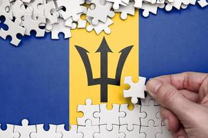 Barbados flag  is depicted on a table on which the human hand folds a puzzle of white color photo