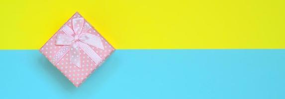 Small pink gift box lie on texture background of fashion pastel blue and yellow colors paper in minimal concept photo