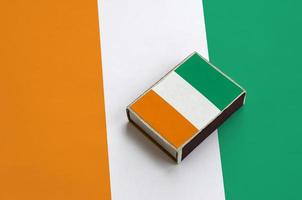 Ivory Coast flag  is pictured on a matchbox that lies on a large flag photo