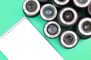 Several photographic lenses and white notebook lie on a bright turquoise background. Copy space photo