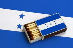 Honduras flag  is shown in an open matchbox, which is filled with matches and lies on a large flag photo