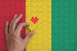 Guinea flag  is depicted on a puzzle, which the man's hand completes to fold photo