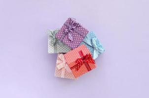 Pile of a small colored gift boxes with ribbons lies on a violet background. Minimalism flat lay top view photo