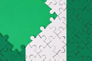 Nigeria flag  is depicted on a completed jigsaw puzzle with free green copy space on the left side photo