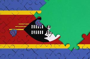 Swaziland flag  is depicted on a completed jigsaw puzzle with free green copy space on the right side photo
