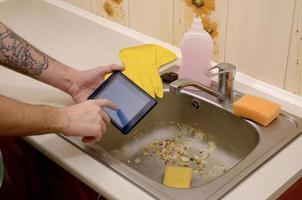 The landlord uses the tablet to call a cleaner in order to clean the clogged kitchen sink photo