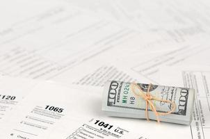 Tax forms lies near roll of hundred dollar bills. Income tax return photo