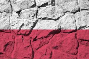 bandera de polonia representada en colores de pintura en el primer plano de la pared de piedra antigua. banner texturizado sobre fondo de pared de roca foto
