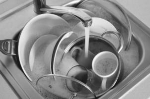 Dirty dishes and unwashed kitchen appliances lie in foam water under a tap from kitchen faucet photo