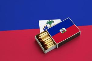 Haiti flag  is shown in an open matchbox, which is filled with matches and lies on a large flag photo