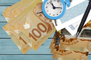100 Canadian dollars bills and alarm clock with pen and envelopes. Tax season concept, payment deadline for credit or loan. Financial operations using postal service photo