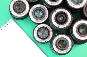 Several photographic lenses and white notebook lie on a bright turquoise background. Copy space photo