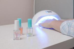 tres botellas de esmalte de uñas transparentes e incoloras en el fondo de manos femeninas en gel uv lámpara blanca de uñas led para secado de manicura foto