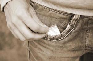 Male hand retrieving drug packet our of blue jean pocket with copy space on abandoned building background photo