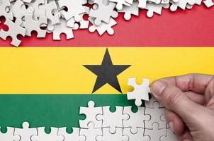 Ghana flag  is depicted on a table on which the human hand folds a puzzle of white color photo