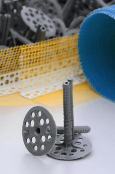 A set of construction items for the insulation of walls. Plastic dowels, a roll of mesh for the insulation of facades and a corner profile with a grid lie on the foam polystyrene surface photo