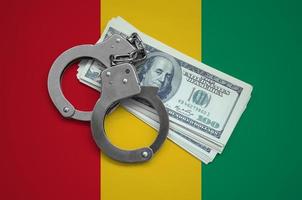 Guinea flag  with handcuffs and a bundle of dollars. Currency corruption in the country. Financial crimes photo