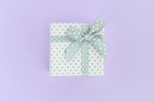 Small white gift box with ribbon lies on a violet background. Minimalism flat lay top view photo