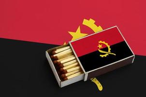 Angola flag  is shown in an open matchbox, which is filled with matches and lies on a large flag photo