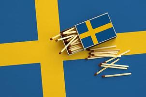 Sweden flag  is shown on an open matchbox, from which several matches fall and lies on a large flag photo